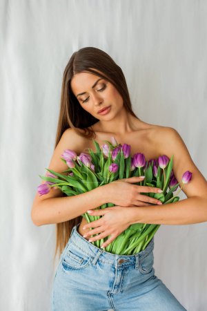 Téléchargez les photos : Portrait de belle jeune femme sexy aux cheveux longs. Modèle avec un bouquet de tulipes lilas sur blanc. Vacances. - en image libre de droit