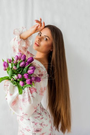 Téléchargez les photos : Portrait of sexy beautiful young woman with long hair. Model with a bouquet of lilac tulips on white. Holidays. - en image libre de droit