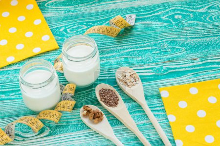 Foto de Yogurt con cinta métrica, cucharas de madera con semillas de lino, nuez, cereales, copos de avena - Imagen libre de derechos