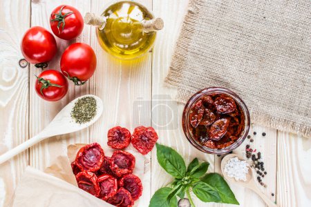 Téléchargez les photos : Fruits de tomate, tomates séchées en papier artisanal, tomates séchées en pot, huile d'olive en saucière, basilic et herbes dans une cuillère en bois sur une table en bois. vue de dessus - en image libre de droit