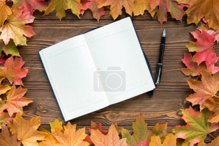 Tagebuch und Stift mit abgefallenen Blättern auf Holzgrund, Draufsicht, Kopierraum. Freiraum für Text