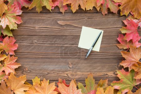 una hoja de papel para notas y pluma con hojas caídas sobre fondo de madera, vista superior, espacio para copiar. espacio libre para texto