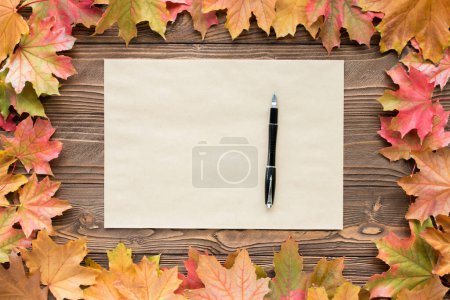une feuille de papier artisanal et un stylo avec des feuilles tombées sur fond en bois, vue de dessus, espace de copie. espace libre pour le texte