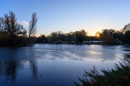 Foto de Un lago congelado al atardecer. Hay hielo en la superficie del lago en esta escena invernal. Un frío día de invierno en Kelsey Park, Beckenham, Kent, Reino Unido. - Imagen libre de derechos