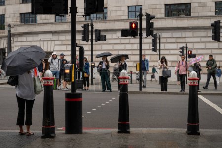 Photo for London, UK: People waiting to cross the road at a pedestrian crossing in the rain. On Victoria Embankment near Blackfriars station in the City of London. - Royalty Free Image