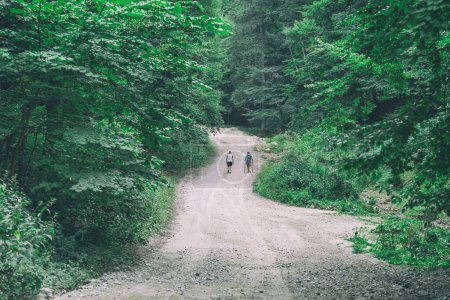 Two hikers walking on the gravel forest road in the mountains of Romania.
