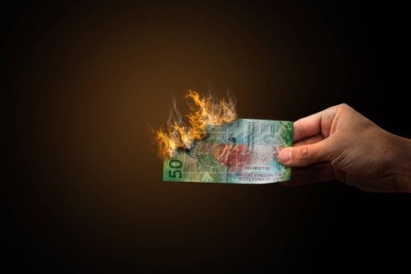 Foto de Hand holding burning 50 Swiss franc banknotes. Recession or inflation concept. - Imagen libre de derechos