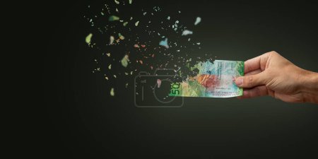 Foto de Inflación de billetes de francos suizos que desaparecen en nada. Mano de hombre sosteniendo 50 francos suizos dispersándose en el aire o nada. - Imagen libre de derechos