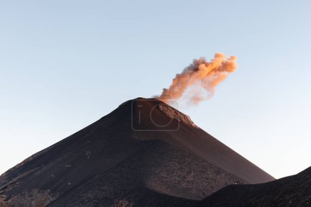 Nahaufnahme eines Vulkanausbruchs mit orangefarbener Rauchsäule bei Sonnenaufgang, klarer Tag in der Nähe von Antigua, Guatemala, Mittelamerika.