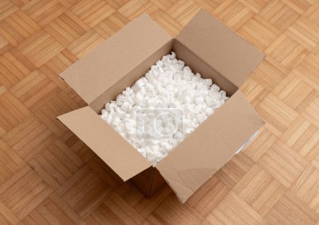 cardboard box packaging with polystyrene pellets inside on wooden floor.
