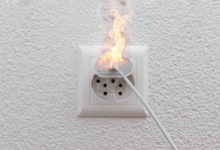 Foto de Enchufe o enchufe de cable cargador de teléfono en llamas de mal funcionamiento en interior, cortocircuito eléctrico que causa fuego en el enchufe. - Imagen libre de derechos