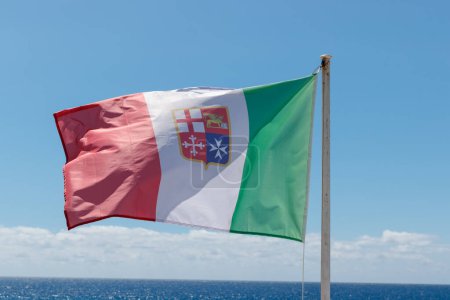 Flagge der italienischen Marine Marina Militare vor blauem Himmel mit Ozean am Horizont.