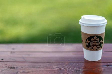 Photo for Istanbul, Turkey - September 3, 2023 : A cup of Starbucks hot beverage coffee on wooden bench. Famous Logo Mermaid - Royalty Free Image