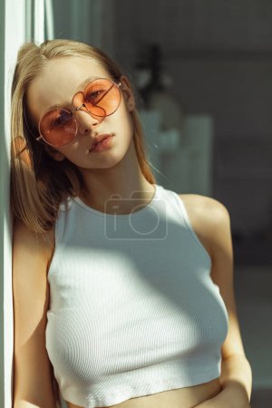 Photo for Young blonde girl with pink sunglasses. Indoor portrait with soft sunlight. Pretty babyface model - Royalty Free Image