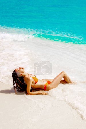 Téléchargez les photos : Femme portant un bikini orange allongé sur une plage tropicale en été. Jolies dreadlocks brune posant en bikini - en image libre de droit