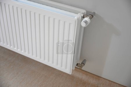 Téléchargez les photos : Un radiateur blanc attaché à un mur, apportant chaleur et confort à la pièce. Sa surface lisse et sa couleur neutre se fondent parfaitement dans le décor environnant - en image libre de droit
