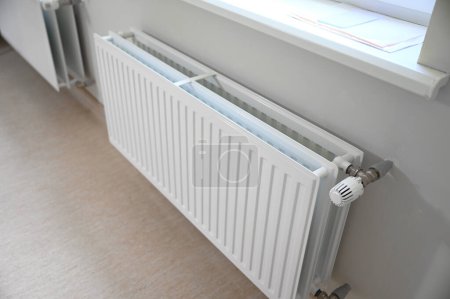 A white radiator attached to a wall, providing warmth and comfort to the room. Its smooth surface and neutral color blend seamlessly into the surrounding decor