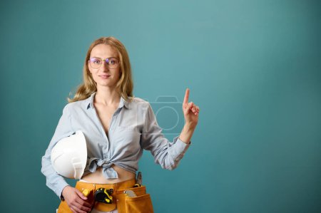 Photo for Young female worker with tool belt holding an instrument in hands isolated on background. Pretty caucasian female with tools planning new project. Portrait in studio. Copy space. - Royalty Free Image