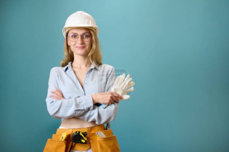 Photo for Portrait of young female worker with tool belt with crossed hands isolated on background. Pretty caucasian female with tools planning new project. Portrait in studio. Copy space. - Royalty Free Image