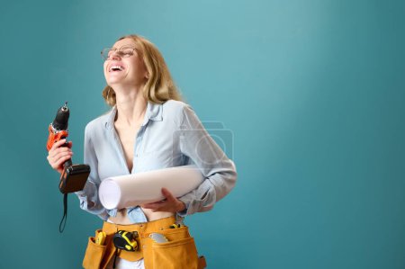 Photo for Young female worker with protective helmet holding a house plan in hands isolated on background. Pretty smilling caucasian female architect are planning new project. People work on architecture project - Royalty Free Image
