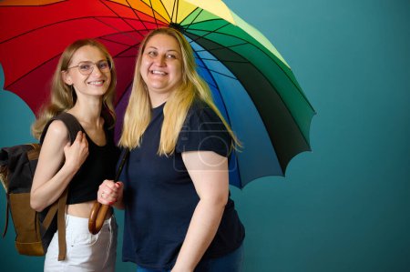Foto de Dos jóvenes lesbianas felices se abrazan bajo un colorido paraguas. Atractivo apoyo femenino, pareja de lesbianas de pie y abrazos. - Imagen libre de derechos