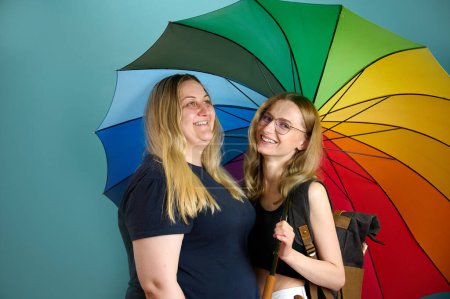 Téléchargez les photos : Deux jeunes filles lesbiennes heureuses s'embrassent sous un parapluie coloré. attrayant soins soutien féminin, couple lesbien debout et câlins. - en image libre de droit
