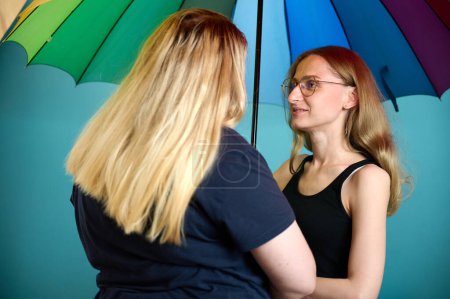 Photo for Two happy young lesbian girls hug under a colorful umbrella. Attractive carring female support, lesbian couple standing and hugging. - Royalty Free Image