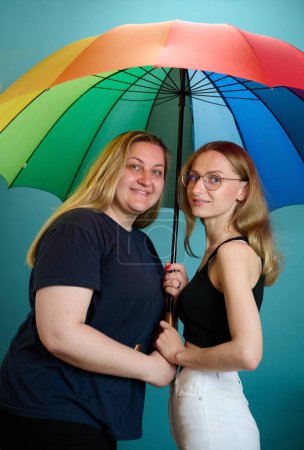 Photo for Two happy young lesbian girls hug under a colorful umbrella. Attractive carring female support, lesbian couple standing and hugging. - Royalty Free Image