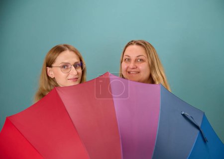 Photo for Two happy young smilling lesbian girls hug behind a colorful umbrella. Attractive carring female support, lesbian couple standing and hugging. - Royalty Free Image