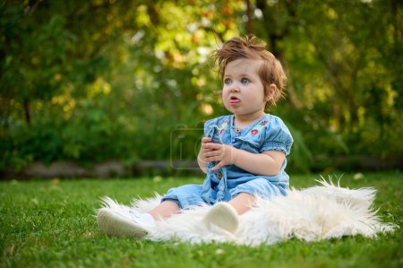 Téléchargez les photos : Adorable fille sur l'herbe dans le jardin. Gros plan portrait. Bonne petite fille dans les paysages d'été. Doux petit enfant à l'extérieur. - en image libre de droit
