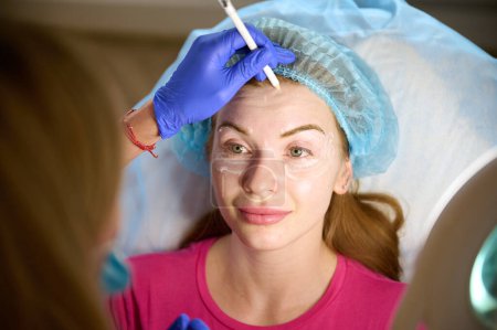 Foto de El cosmetólogo inyecta sustancia en la cara que modifica al paciente para hacer la corrección no quirúrgica. Inyecciones de relleno. Concepto de tratamientos correctivos estéticos. - Imagen libre de derechos