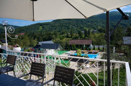 Photo for Wide angle, view of the terrace with a table and an umbrella from the sun. Apartment for rest in the mountains. Resort in Carpathian mountains. - Royalty Free Image