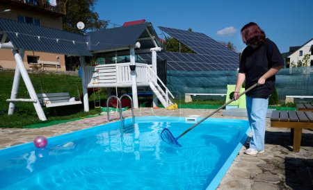 Photo for Enthusiastic cleaner ready to work. Young female holding cleaning equipment for swimming pools. Positive girl cleaning pool by pool skimmer. - Royalty Free Image