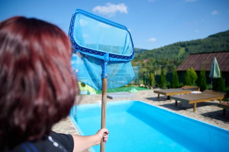 Photo for Young woman cleans swimming pool. Personnel cleaning the pool from leaves in sunny summer day. Hotel staff worker cleaning the pool. Cleaning swimming pool service. Purification with a net. - Royalty Free Image