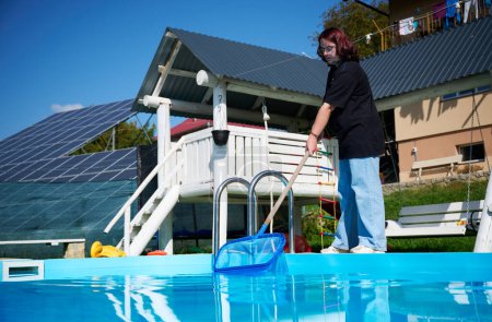 Photo for Young woman cleans swimming pool. Personnel cleaning the pool from leaves in sunny summer day. Hotel staff worker cleaning the pool. Cleaning swimming pool service. Purification with a net. - Royalty Free Image