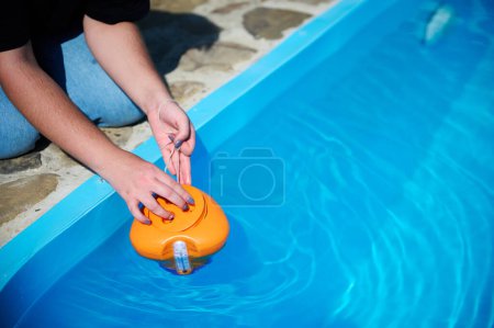 Photo for White mini chlorine tablet in dispenser for disinfection of swimming pool. Pool cleaner putting new chlorine tablet to feeder. Bright orange dispenser on surface of swimming pool. - Royalty Free Image