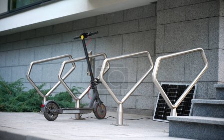 Téléchargez les photos : Scooter électrique garé dans un parking moderne près de la maison avec recharge à partir d'un panneau solaire - en image libre de droit