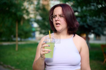 Photo for Pretty girl drinking lemonade at sunny day. Young female does not agree with something, a look of displeasure on her face. Positive girl drinking and relaxing outside. - Royalty Free Image