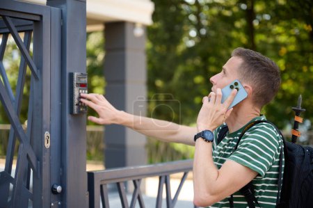 Téléchargez les photos : L'homme ouvre la porte à la cour. Jeune homme appelant le propriétaire pour demander le code. Curieux touriste essayant d'ouvrir la porte de l'hôtel. Ivano-frankivsk, Ukraine - 09.07.2023 - en image libre de droit