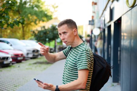 Photo for Confused traveler trying to find right way. Young male can't understand where to go. Attractive man checking map on his phone. - Royalty Free Image