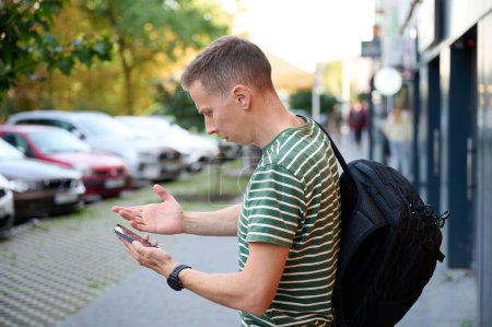 Photo for Confused traveler trying to find right way. Young male can't understand where to go. Attractive man checking map on his phone. - Royalty Free Image