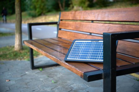 Foto de Panel solar portátil en el banco del parque. Energía renovable. - Imagen libre de derechos