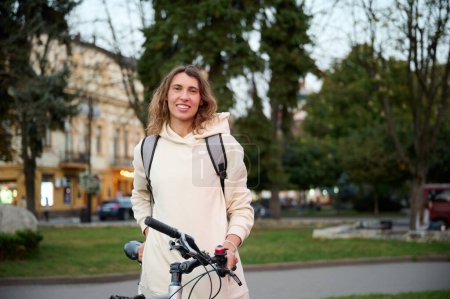 Photo for Close-up portrait of woman with backpack and bicycle walking through the city and along the embankment in the evening at sunset. - Royalty Free Image