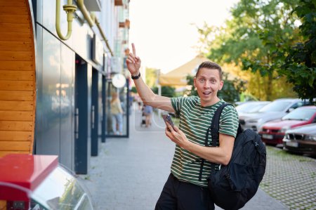 Photo for Excited man finally found his hotel. Happy man pointing on building he was looking for. Young male points finger up. - Royalty Free Image