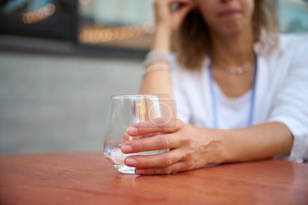 Foto de Retrato de una joven atractiva mujer de negocios sentada en una mesa en un café y sosteniendo un vaso de agua transparente. Vista de cerca. - Imagen libre de derechos