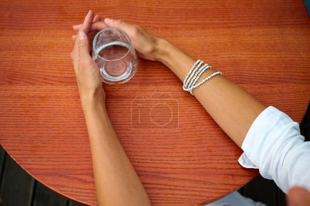 Téléchargez les photos : Portrait d'une jeune femme d'affaires attrayante assise à une table dans un café et tenant un verre d'eau transparent. Vue rapprochée. - en image libre de droit