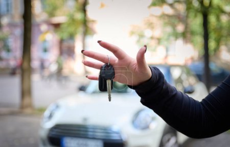 Photo for Woman holding key against blurred automobile, closeup. Car keys, car sales, car sales. Successful employee holding modern car key in female hand - Royalty Free Image