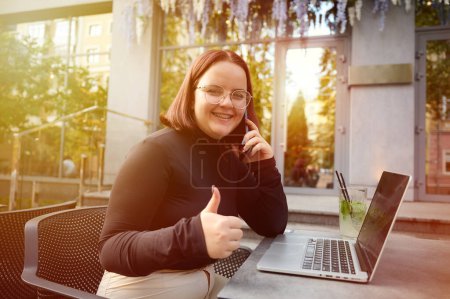 Photo for Portrait of smilling young student girl working remotely from laptop while sitting at a table in a cafe. Female student studying at park using modern laptop at bright sunny day. Working outdoor. - Royalty Free Image