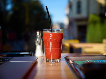 Foto de Vista de cerca del vaso lleno de jugo de tomate en la mesa en la cafetería al aire libre. Un día soleado brillante. Apetitivo jugo de tomate en un vaso - Imagen libre de derechos