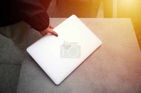 Foto de Primer plano de la mano de una mujer poniendo un portátil gris en la mesa. Dispositivos modernos para el trabajo y el ocio. Funda Apple Macbook Pro Retina en un escritorio. Ivano-Frankivsk, Ucrania - 10.21.2023 - Imagen libre de derechos